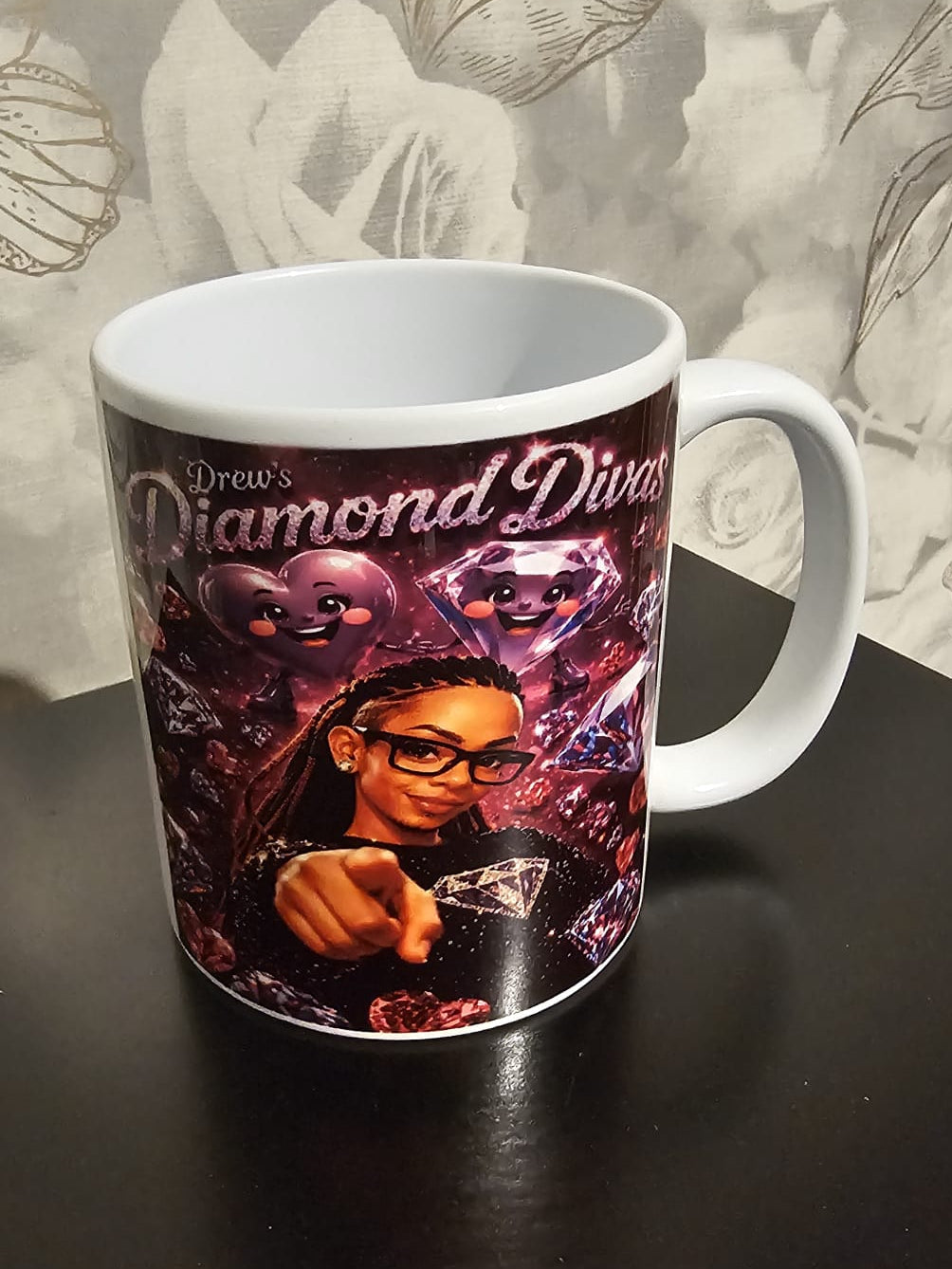 Mug with 'Drew's Diamond Divas' design on a dark surface with a floral patterned background